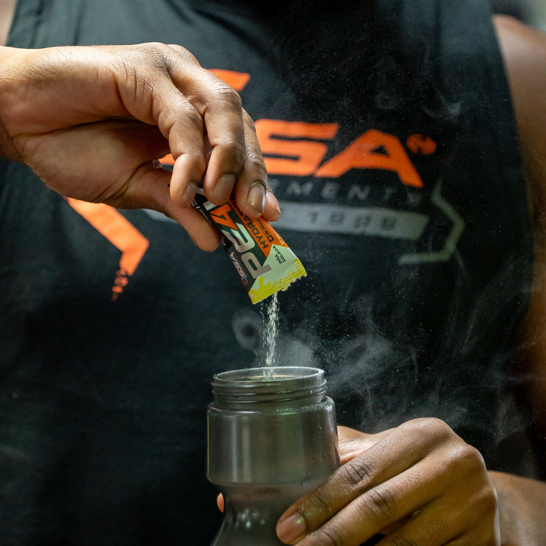 Person adding a packet to a container with steam, wearing a black shirt with orange text.